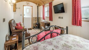 A cozy room with a bed, a chair, a table, a television, and a fireplace. - Shepherds Hut - UK45529 (Leighton, near Shrewsbury)
