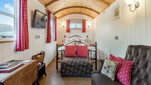 A cozy room with a wooden ceiling, a bed with floral bedding, a leather sofa, and a desk with a chair. - Shepherds Hut - UK45529 (Leighton, near Shrewsbury)