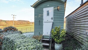 A small, single-story building with a white door and a small window, surrounded by a garden with frost-covered plants. - Shepherds Hut - UK45529 (Leighton, near Shrewsbury)