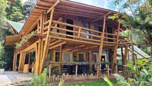 A multi-story bamboo structure with a balcony, outdoor seating area, and a garden with various plants. - Refugio en el Bosque (Envigado)