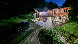 A modern wooden house with a spacious patio, a car parked in front, and a well-maintained garden. - Refugio en el Bosque (Envigado)