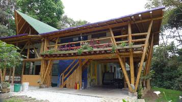 Un edificio de madera con techo verde, un balcón lleno de flores y una escalera que lleva a la entrada.