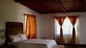 Un dormitorio con cama, techo de madera y dos ventanas con cortinas.