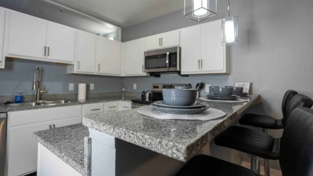 A modern kitchen with white cabinets, a granite countertop, a microwave, and a dining area with black chairs.