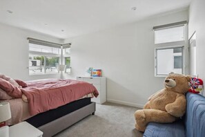 A bedroom with a bed, a large teddy bear, a blue sofa, and a window.