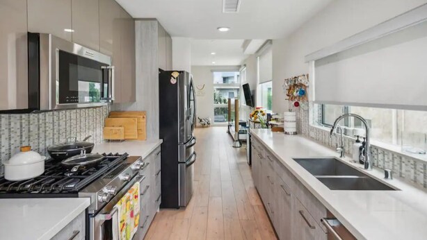 A modern kitchen with stainless steel appliances, a double sink, and a view to the living area. - Close to Hollywood and Getty with a Panorama Deck (Los Angeles)