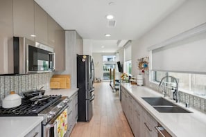 A modern kitchen with stainless steel appliances, a double sink, and a view to the living area.