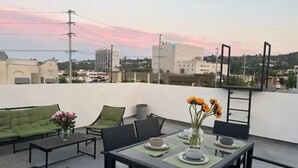 A rooftop terrace with outdoor seating, a table set for dining, and a cityscape view in the background. - Close to Hollywood and Getty with a Panorama Deck (Los Angeles)