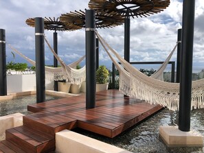 Un hamac orné de franges en macramé, une terrasse en bois et des plantes en pot.