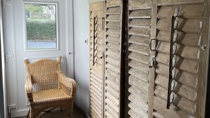 A hallway with a wicker chair, wooden shutters, and a door with a window.