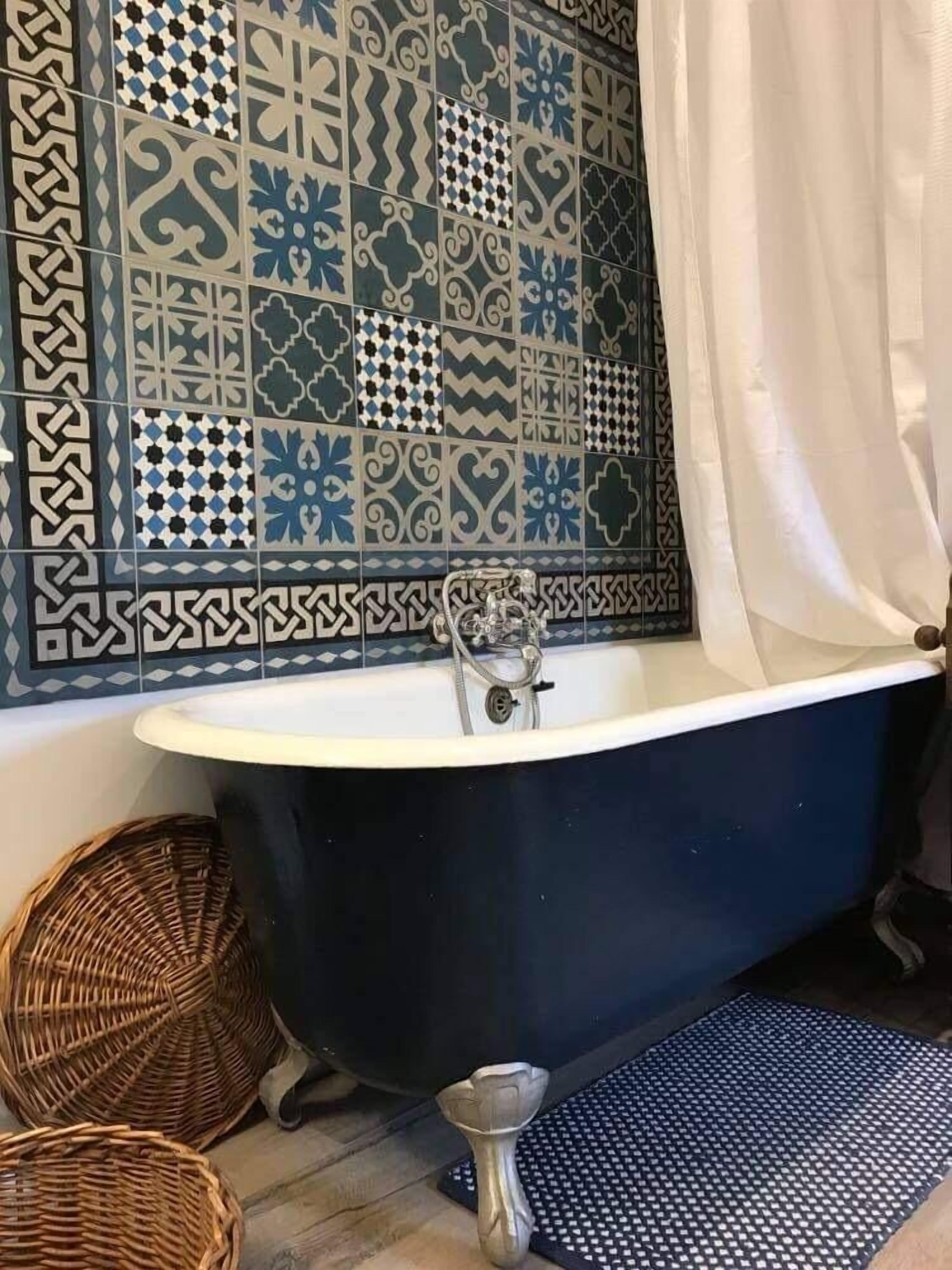 A bathroom with a freestanding bathtub, patterned tiles, a shower curtain, and two wicker baskets.
