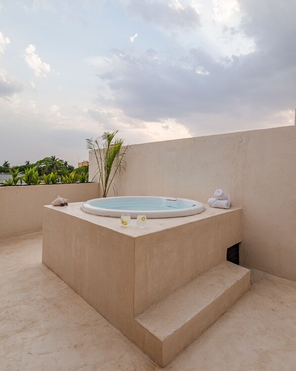 A hot tub on a rooftop terrace with a view of palm trees and a cloudy sky.