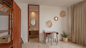 Ein modernes Zimmer mit einem Holzschrank, einem Schreibtisch mit Stuhl, einer Zimmerpflanze und einem durchgegangenen Tür erkennbaren Badezimmer.