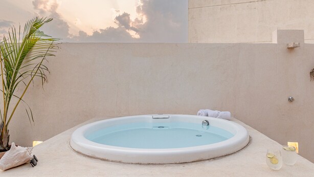 Ein Whirlpool mit freiem Blick auf Himmel und Wolken, einer Zimmerpflanze und einem Handtuch am Rand.