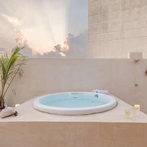 A hot tub with a clear view of the sky and clouds, a palm plant, and a towel on the edge.
