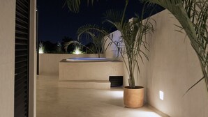 Ein Außenbereich bei Nacht mit Betonboden, einer kleinen Wasseranlage und Topfpflanzen.