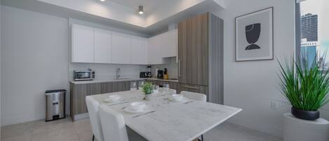 Een moderne keuken met witte kasten, een eettafel gedekt voor vier personen en een potplant.