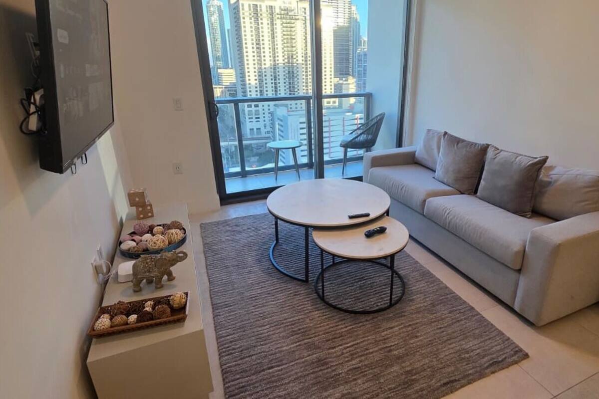 Ein modernes Wohnzimmer mit einer Couch, zwei Couchtischen, einem Flachbildfernseher und einem Balkon mit Blick auf die Stadt.