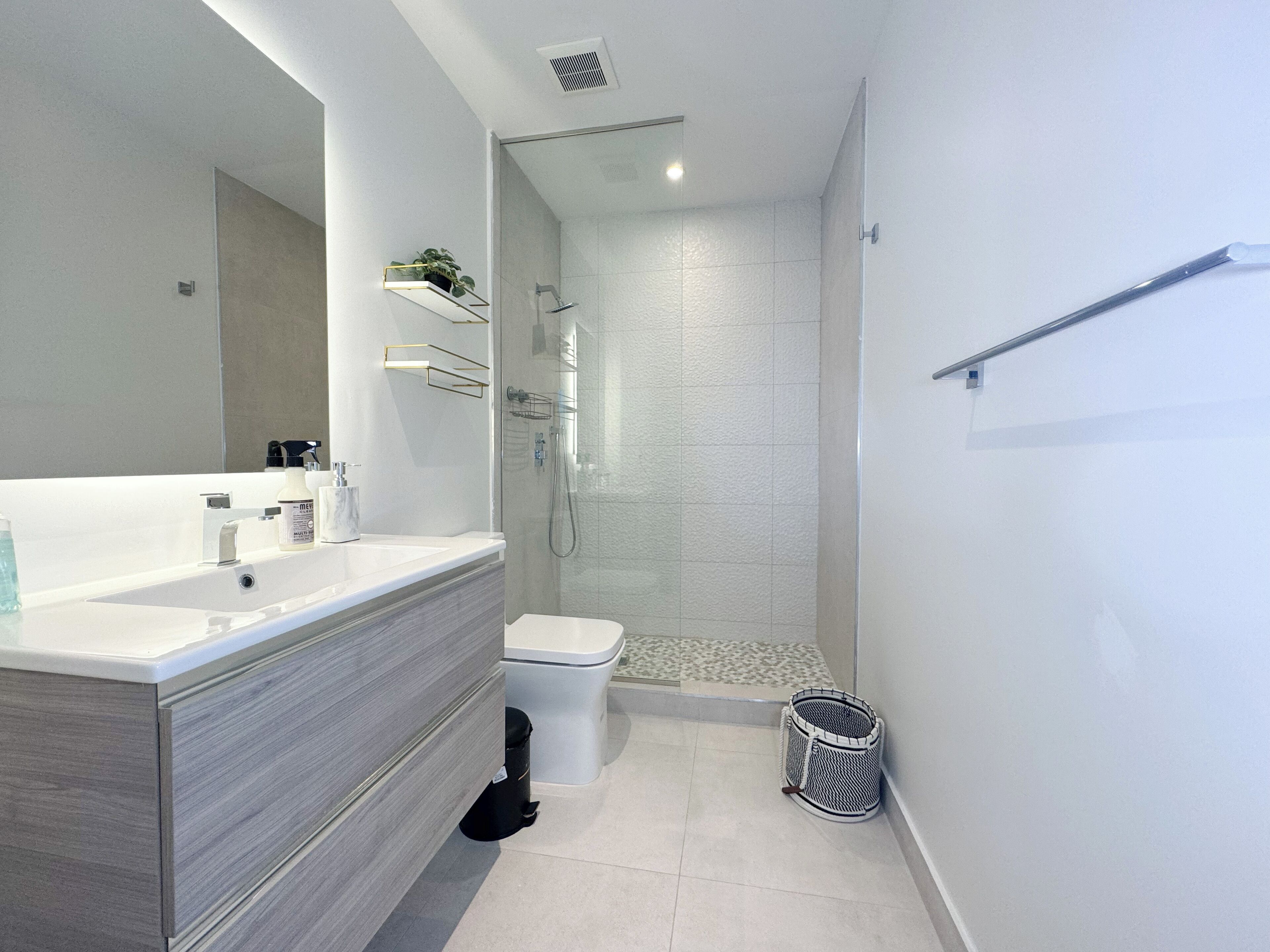 A modern bathroom with a large mirror, a white sink, a toilet, and a glass-enclosed shower.