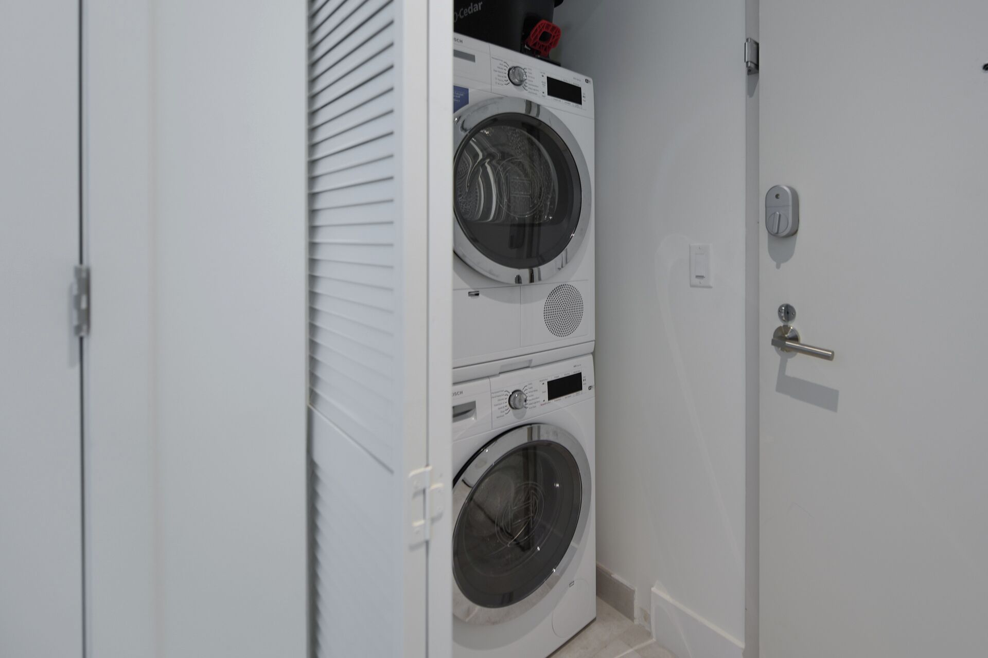 A compact laundry room with two stacked front-loading washing machines and a door with a handle.