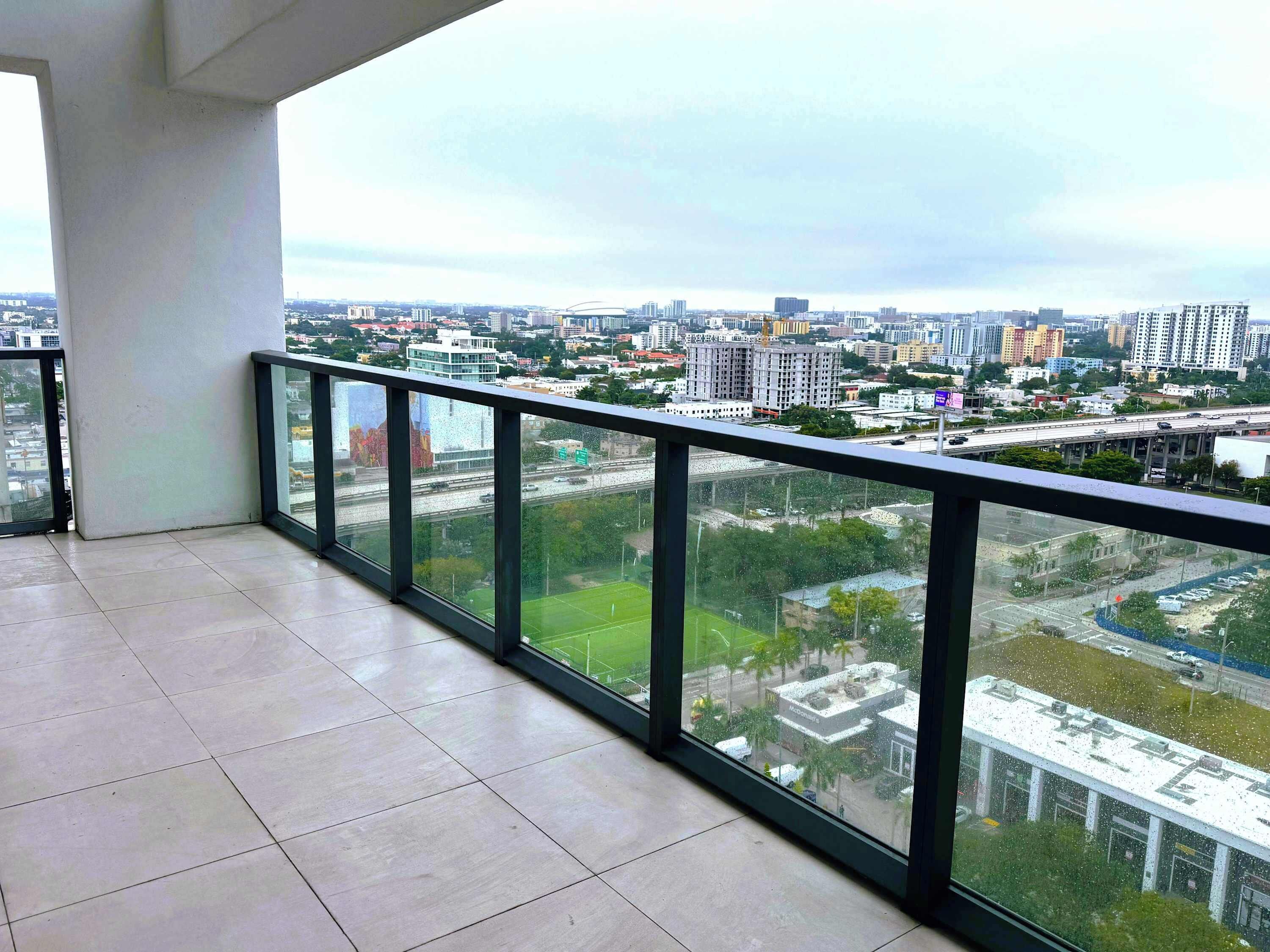 A balcony with a city view, tiled floor, and a glass railing.