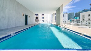 Une piscine intérieure à l’eau d’un bleu cristallin, entourée d’une terrasse en béton et d’une rambarde en verre.