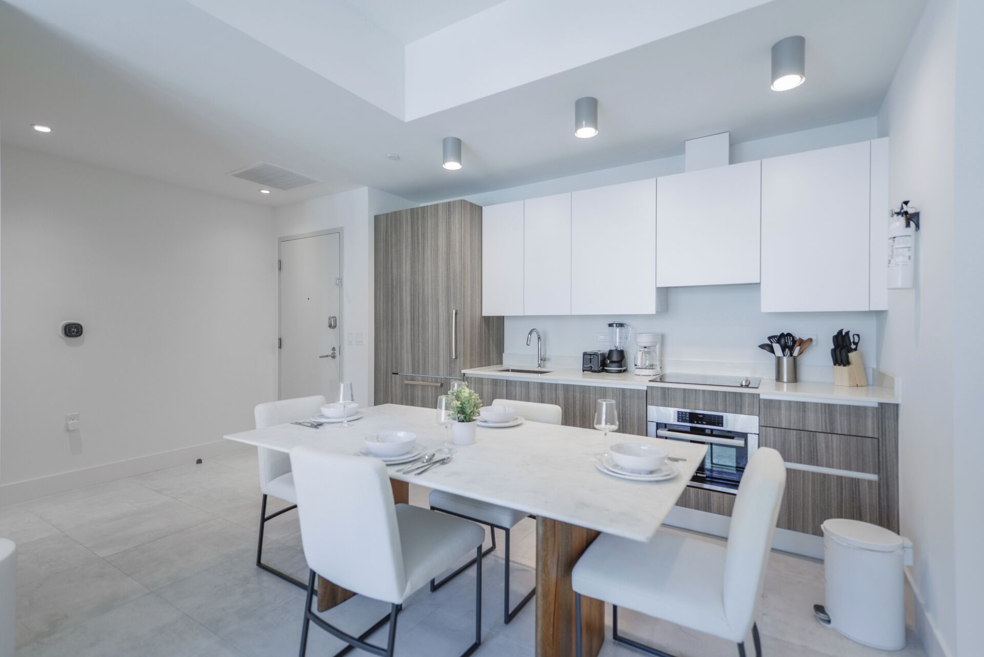 Een moderne keuken met witte kasten, een ingebouwde oven en een eethoek met een witte tafel en stoelen.