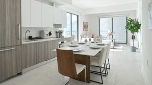 Une cuisine moderne avec des meubles blancs, un coin repas doté d’une table blanche pour quatre personnes, et une grande fenêtre offrant une vue sur la ville.