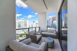 Ein Balkon mit Korbmöbeln und einem runden Tisch, mit Blick auf eine Skyline mit Hochhäusern.