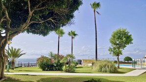 A well-maintained garden with palm trees, a swimming pool, and a clear view of the sea. - SR Almirante 1ª Linea de Playa (Mijas)