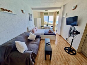 Une chambre d’hôtel avec un lit, un canapé, une petite table, une télévision et un ventilateur.