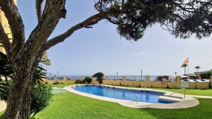 A swimming pool surrounded by well-maintained grass, a tree, and a view of the sea. - SR Almirante 1ª Linea de Playa (Mijas)