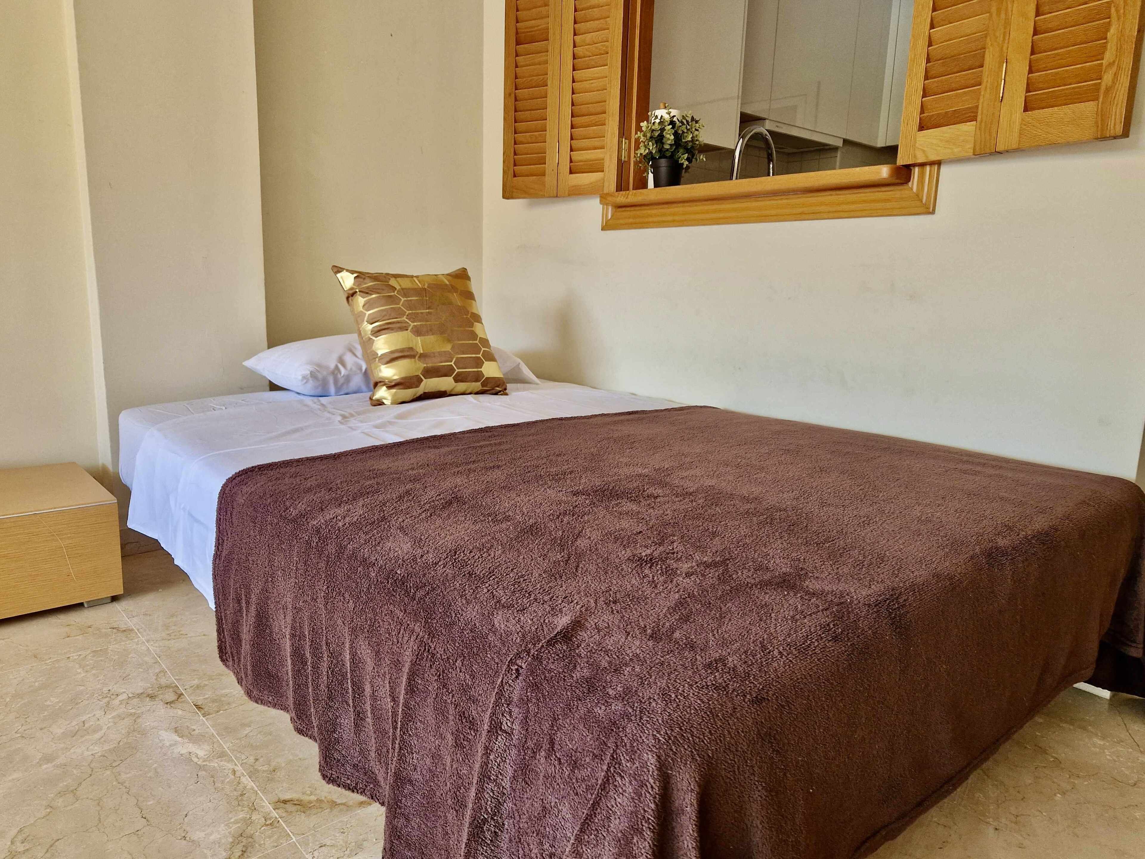 Una camera da letto con un letto, un comodino in legno, una coperta marrone, un cuscino bianco e una persiana di legno.