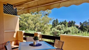 Eine Terrasse mit Tisch und Stühlen, einem kleinen Topfpflanzen und Blick auf Bäume und Gebäude.