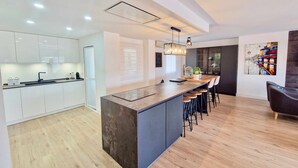 A modern kitchen with a central island, bar stools, and a dining area with a large window. - SR Penthouse Parque Olivar Torremolinos (Torremolinos)