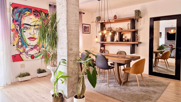 A modern living room with a dining area, featuring a large abstract painting, multiple potted plants, and a wooden dining table with chairs. - SR Penthouse Parque Olivar Torremolinos (Torremolinos)