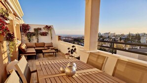 A balcony with a wooden table, a sofa, and potted plants. - SR Penthouse Parque Olivar Torremolinos (Torremolinos)