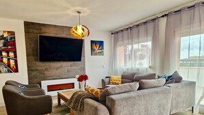 A modern living room with a grey sofa, a black armchair, a wooden coffee table, and a flat-screen TV mounted on the wall. - SR Penthouse Parque Olivar Torremolinos (Torremolinos)