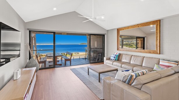 A modern living room with a large sliding glass door leading to a balcony with a view of the sea.