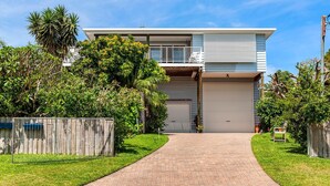 A two-story house with a garage, surrounded by a wooden fence and lush greenery. - Shoal Bay Riggers - 7  Rigney St, Shoal Bay (Shoal Bay)