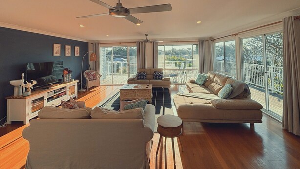 A spacious living room with a large TV, comfortable seating, and a balcony with a view. - Shoal Bay Riggers - 7  Rigney St, Shoal Bay (Shoal Bay)