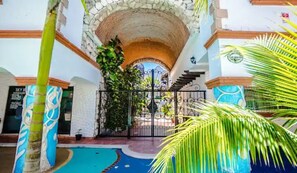 Enter a tranquil oasis through our traditional stone archway, surrounded by lush greenery and a vibrant mural.