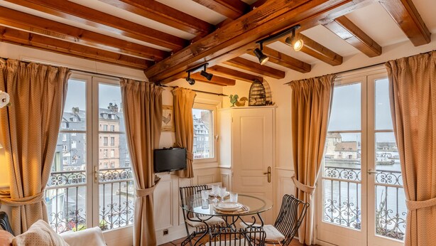 A cozy room with a balcony, wooden beams, a dining table with chairs, and a TV on the wall. - Key West - charming studio ON the port of Honfleur - Superb 360° view (Honfleur)