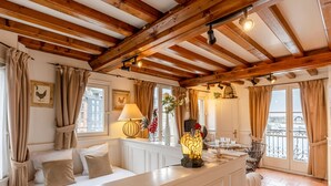 A cozy room with a wooden ceiling, a sofa, a table with a lamp, and a view of the city through large windows. - Key West - charming studio ON the port of Honfleur - Superb 360° view (Honfleur)