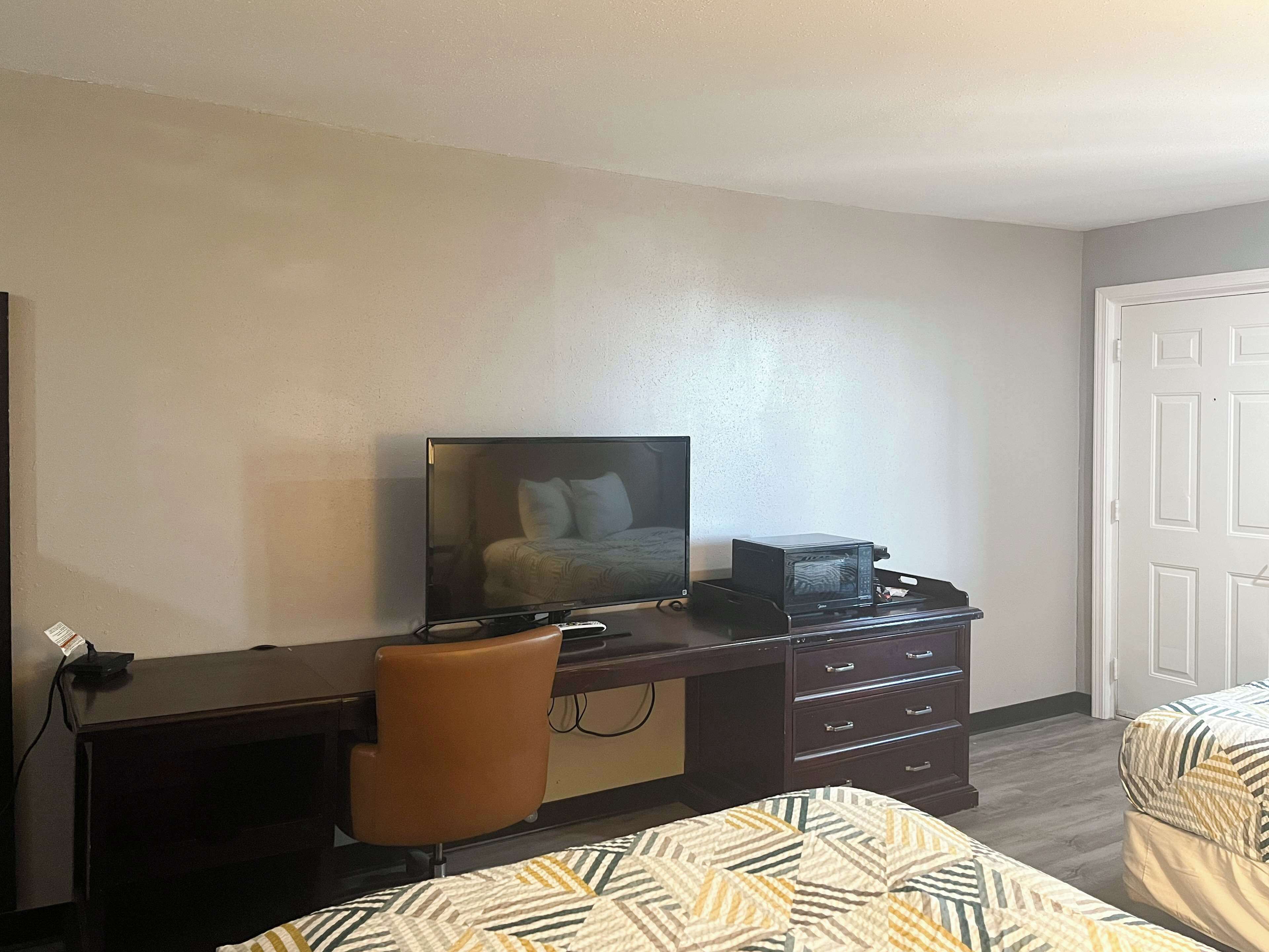 Una habitación de hotel con una cama, un escritorio con televisor, una silla y un microondas.