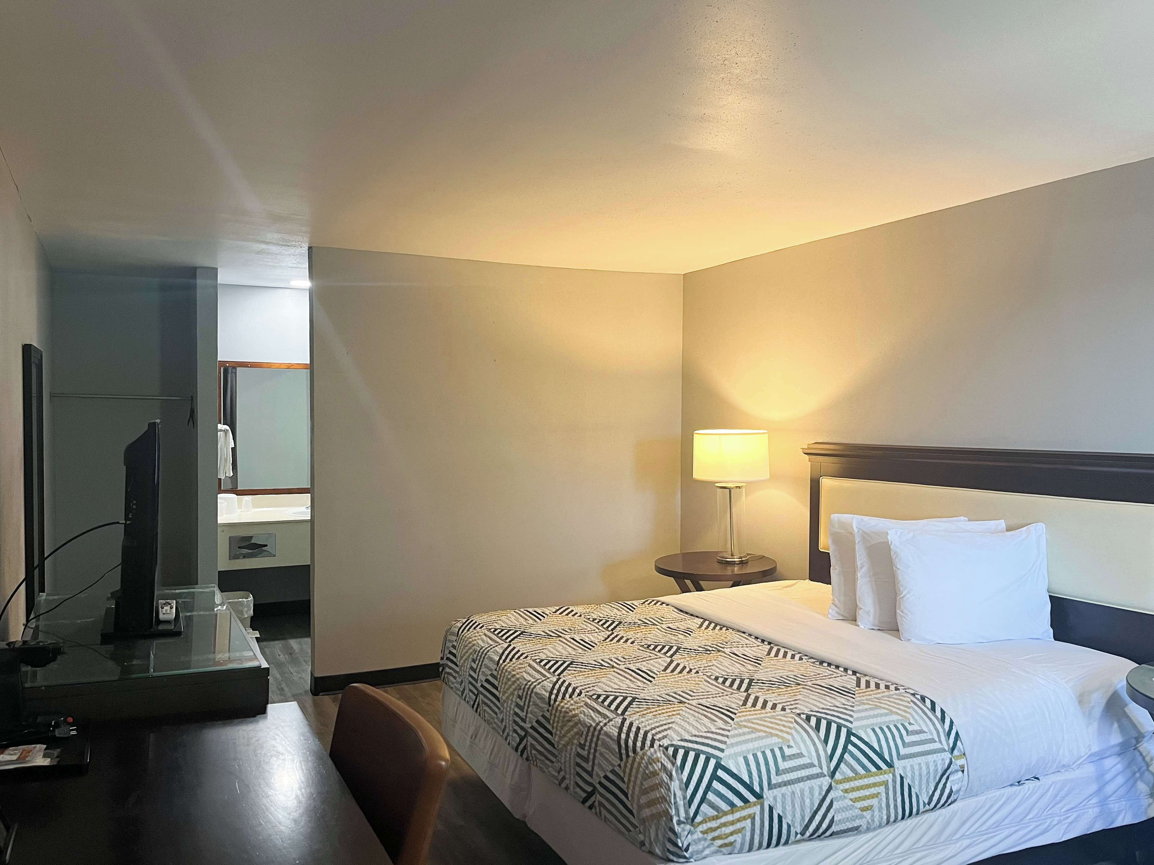 Una habitación de hotel con cama, escritorio, silla, televisión y lámpara.