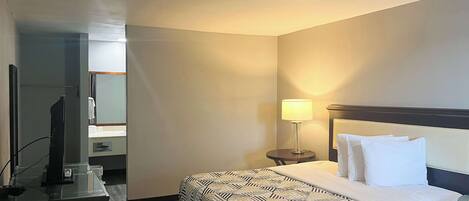 Una habitación de hotel con cama, escritorio, silla, televisión y lámpara.