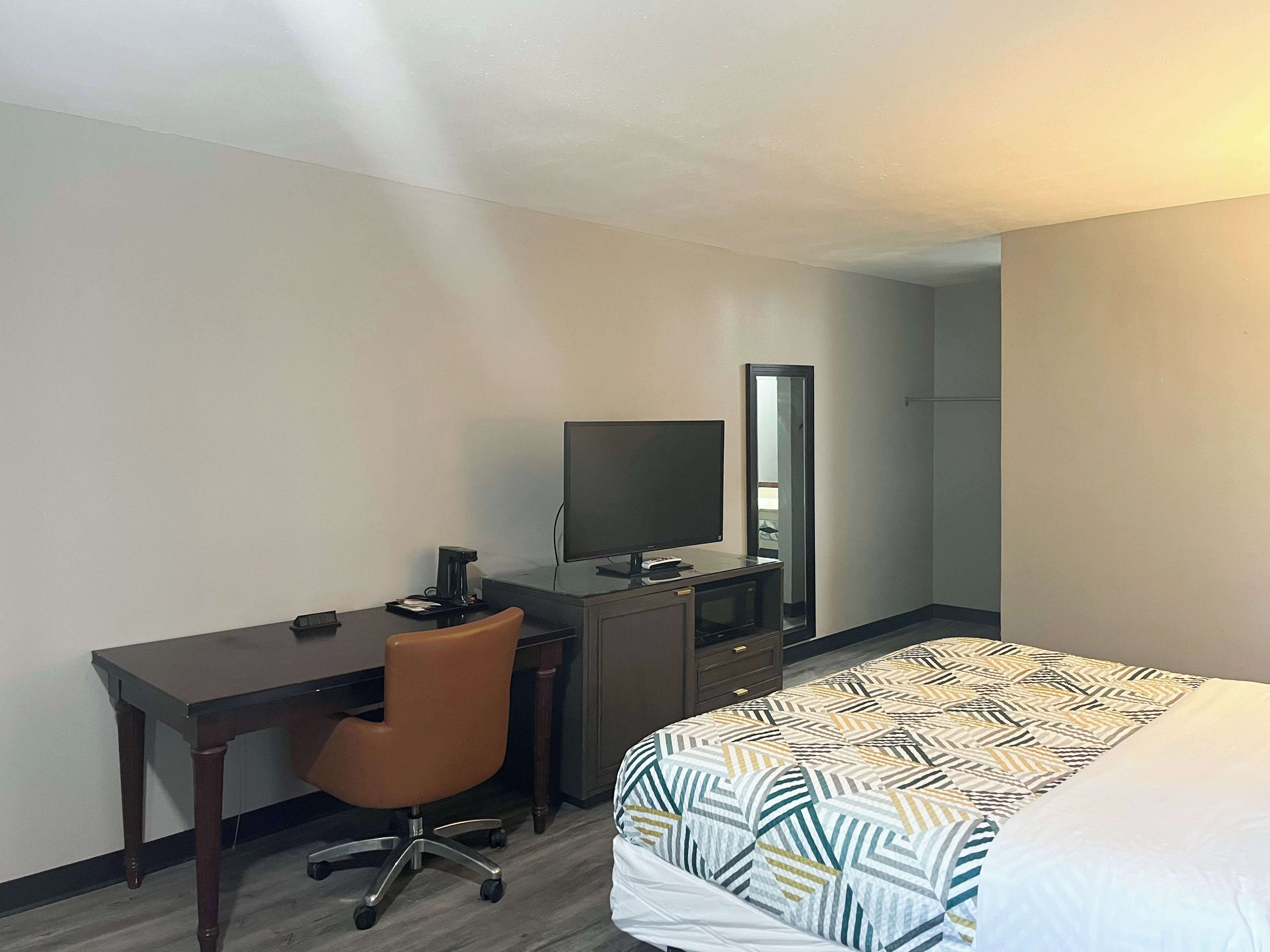 A hotel room with a bed, a desk, a chair, a television, and a mirror.