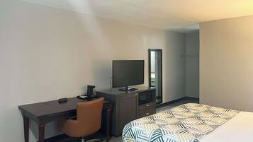 A hotel room with a bed, a desk, a chair, a television, and a mirror.