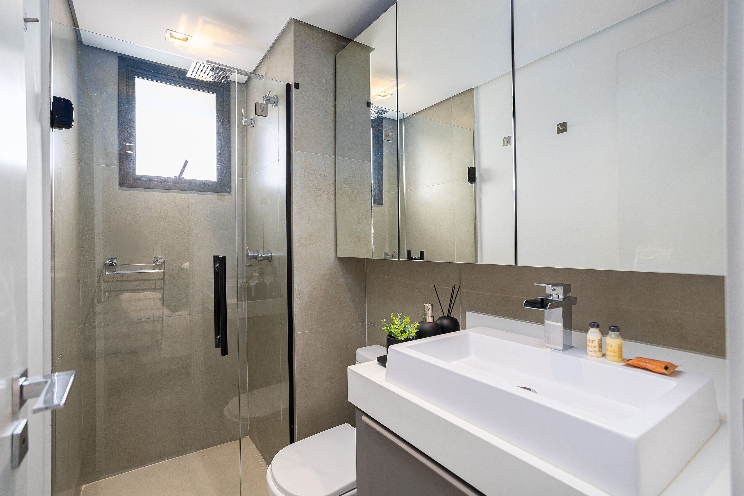 A modern bathroom with a glass shower enclosure, a white sink with a mirror above, and a toilet.
